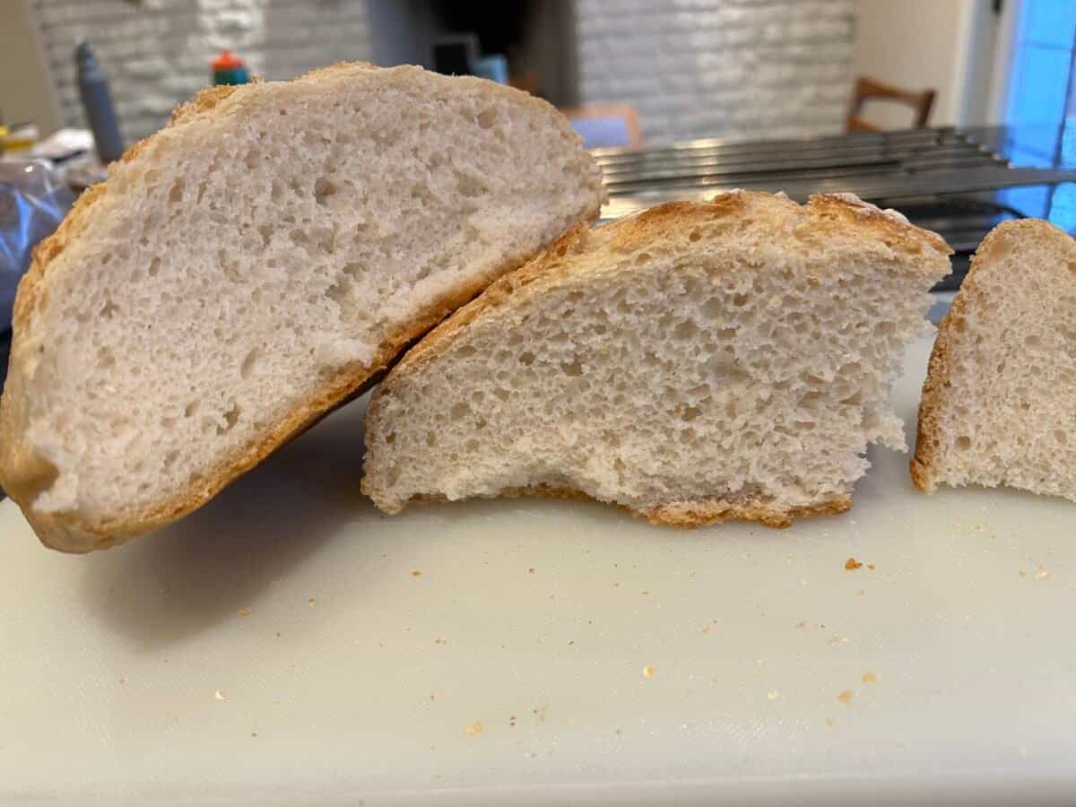 Two pieces of homemade bread with a light, airy crumb and crust are displayed on a cutting board, with a cooling rack and kitchen background visible.