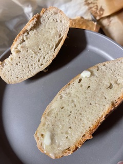 Two slices of No Knead Gluten Free Bread, one with a pat of melted butter, sit on a gray plate. The bread has a light, airy texture and a golden crust.