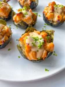 Close-up of crispy seaweed cups, reminiscent of Salmon Sushi Cups, filled with diced, saucy chicken, topped with creamy sauce and garnished with chopped chives, arranged on a white plate.