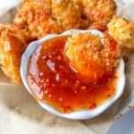 Golden, crispy coconut shrimp—made from our signature Coconut Shrimp Recipe—served in a basket with a small white dish of sweet chili dipping sauce, all nestled on parchment paper.