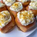 Close-up of golden brown Lazy Cinnamon Buns topped with swirls of white icing and sprinkled with bright yellow-gold sugar crystals, arranged on a white plate.