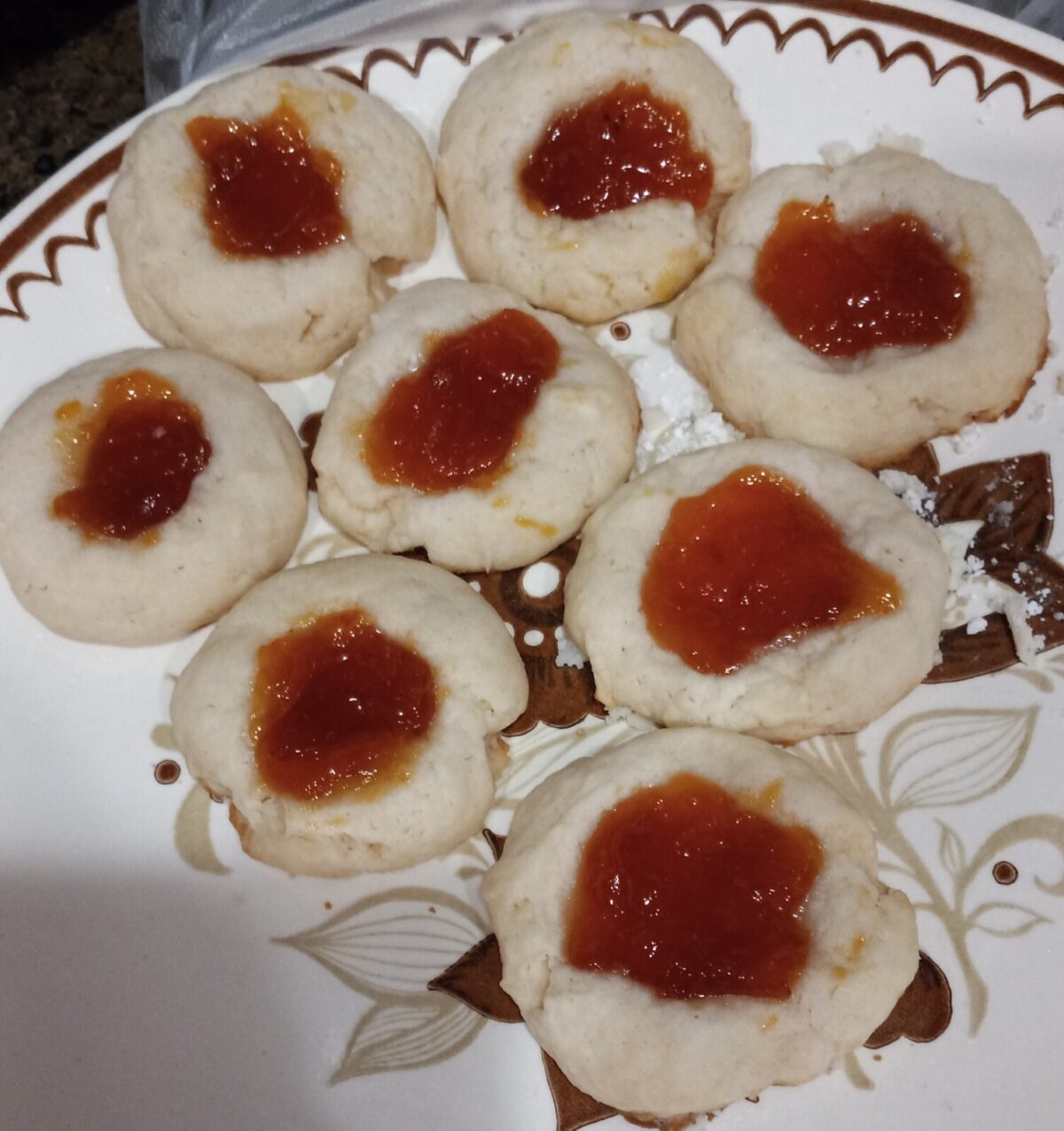 A plate with nine Lemon Cheesecake Thumbprint Cookies filled with red jam, arranged closely together on a decorative dish.