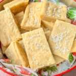 Rectangular Shortbread Cookie Bars with sprinkled white sugar pearls, arranged in a festive tin lined with holiday-themed paper.