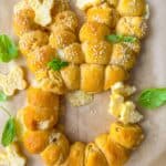 Heart-shaped bread made of small rolls, topped with sesame seeds and butter. Garnished with basil leaves and cheese cut into butterfly shapes. Placed on parchment paper.