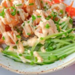 A bowl filled with crispy tofu cubes, shredded carrots, and julienned cucumber, topped with a creamy sauce and chopped chives.