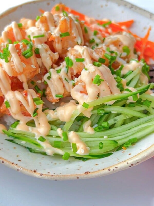 A bowl filled with crispy tofu cubes, shredded carrots, and julienned cucumber, topped with a creamy sauce and chopped chives.