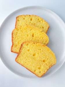 Three slices of golden yellow Whole Orange Blender Cake are arranged on a white plate. The cake appears moist and fluffy, with a slightly browned edge and small air pockets throughout the slices.