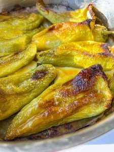 Close-up of roasted yellow-green peppers in a pan, their slightly blistered, browned skin glistening under natural light—perfect for preparing Stuffed Peppers with Feta.