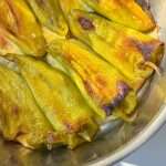 Roasted green chili peppers in a metal dish, with slightly blistered and browned skin, arranged closely together in natural sunlight—perfect for making Stuffed Peppers with Feta.