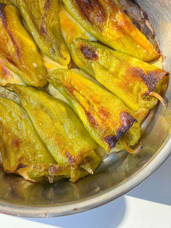 Roasted green chili peppers in a metal dish, with slightly blistered and browned skin, arranged closely together in natural sunlight—perfect for making Stuffed Peppers with Feta.