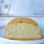 A close-up of two thick slices of moist Healthy Sandwich Bread loaf cake on a white plate, with a bright, blurred kitchen background.
