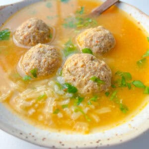 A bowl of Hidden Veggie Meatball Soup with four meatballs, rice, chopped fresh herbs, and a spoon in a light broth.