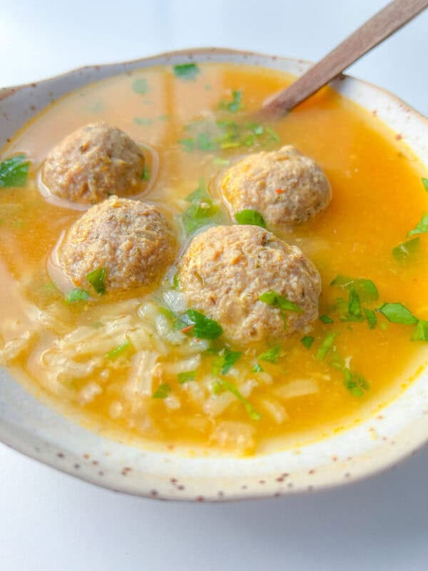 A bowl of Hidden Veggie Meatball Soup with four meatballs, rice, chopped fresh herbs, and a spoon in a light broth.
