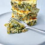 Three stacked slices of oven baked rice casserole with a golden top, served on a white plate with a fork and a small portion of the casserole next to the stack.