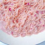 Close-up of Pink Pasta coated in a creamy, pastel pink sauce, garnished with small pink flower petals, served in a white bowl.