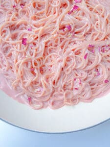 Close-up of Pink Pasta coated in a creamy, pastel pink sauce, garnished with small pink flower petals, served in a white bowl.