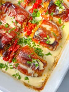 Bulgarian Stuffed Peppers roasted to perfection in a creamy white sauce, topped with chopped fresh parsley. The slightly charred peppers are filled with a golden mixture and served in a white baking dish.