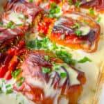 Close-up of baked stuffed tomatoes, inspired by Bulgarian Stuffed Peppers, topped with melted cheese and chopped parsley, all sitting in a creamy white sauce. The cheese is golden brown in spots, and the tomatoes are vibrant red.