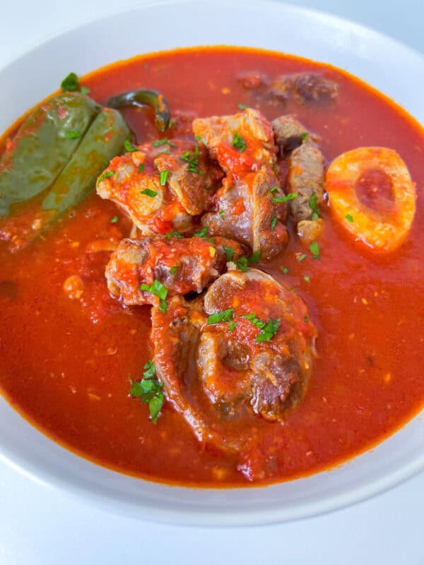 A bowl of rich, red stew with pieces of meat, a hard-boiled egg, a large bay leaf, and chopped herbs in an authentic Italian tomato sauce.