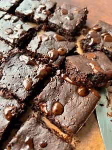 Close-up of sliced, fudgy Black Bean Brownies on parchment paper, topped with melted chocolate chips. A knife is partially visible under one brownie square.
