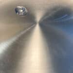 A single drop of oil sits on the shiny surface of a stainless steel frying pan, reflecting light in a circular pattern—a simple step in discovering how to make stainless steel non stick.