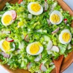 A Simple Green Salad is served in a wooden bowl, featuring chopped lettuce, sliced radishes, and hard-boiled egg slices, accompanied by two wooden salad servers.