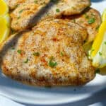Grilled Lemon Chicken breasts garnished with chopped herbs, served on a white plate with lemon wedges on the side.