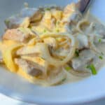 Bowl of creamy stew featuring a classic Liver and Onions Recipe, with tender meat slices, onions, and light sauce, garnished with chopped green herbs and served with a wooden spoon.