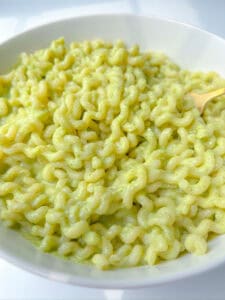 A close-up of a bowl filled with creamy, green Broccoli Ricotta Pasta, likely coated in a pesto or avocado sauce, with a fork partially visible on the right side.