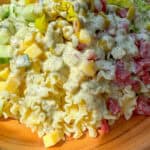 A wooden bowl filled with Grinder Pasta Salad—pasta, diced tomatoes, cucumbers, cheese cubes, olives, pepperoncini, and lettuce—all topped with creamy Italian dressing.