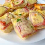 Slices of bread topped with ham and melted cheese create classic Ham and Cheese Sandwiches, garnished with chopped parsley and beautifully arranged on a white plate.