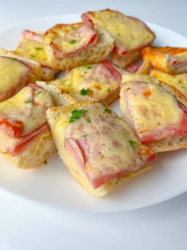 Slices of bread topped with ham and melted cheese create classic Ham and Cheese Sandwiches, garnished with chopped parsley and beautifully arranged on a white plate.
