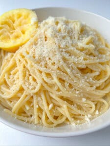 A bowl of Pasta Limone spaghetti topped with grated cheese, served with a slice of lemon on the rim for a fresh, zesty finish.