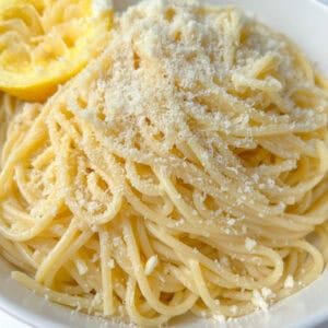 A bowl of Pasta Limone spaghetti topped with grated cheese, served with a slice of lemon on the rim for a fresh, zesty finish.