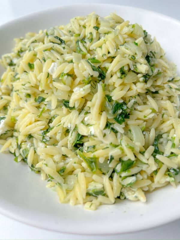 A close-up of a plate of Spinach Orzo Salad, featuring orzo pasta mixed with fresh herbs and a light, creamy sauce, served on a white dish.