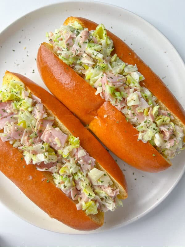 Two soft sandwich rolls filled with a creamy Italian Chopped Sandwich mixture of ham, lettuce, and herbs are served on a white plate.