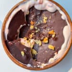 A wooden bowl filled with strawberry yogurt topped with a layer of dark chocolate and sprinkled with chopped walnuts. The chocolate is cracked, revealing the creamy Strawberry Yogurt Bowl beneath.