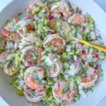 A bowl of Creamy Shrimp Salad with chopped celery, red onion, and fresh dill, all mixed together and served with a yellow serving spoon.