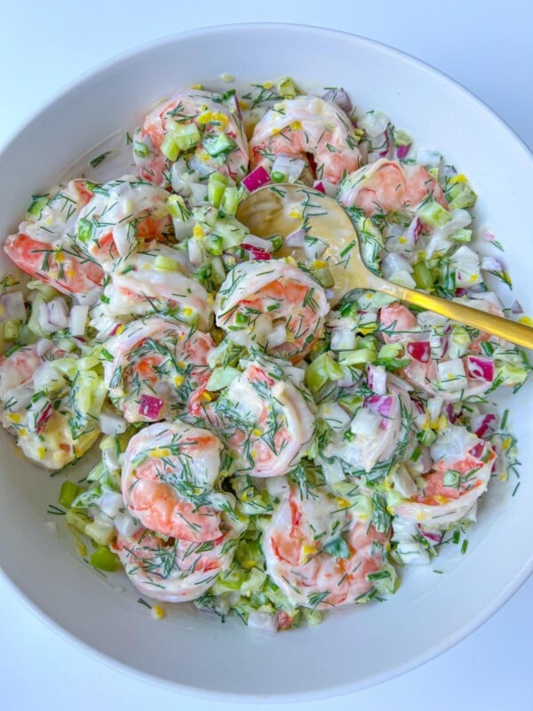 A bowl of Creamy Shrimp Salad with chopped celery, red onion, and fresh dill, all mixed together and served with a yellow serving spoon.