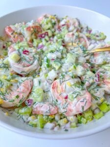 A close-up of a Creamy Shrimp Salad with chopped cucumbers, red onions, dill, and other fresh vegetables, all mixed together in a white bowl.