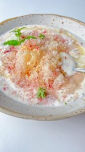 A bowl of yogurt topped with crushed ice, honey, and fresh mint leaves, reminiscent of a refreshing Peaches and Cream Dessert, with a spoon resting in the bowl.