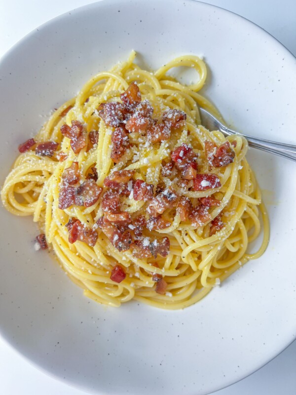A plate of classic Carbonara topped with crispy pancetta and grated cheese, served on a white dish with a fork.