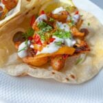 A soft tortilla filled with seasoned grilled chicken, sliced bell peppers, fresh herbs, and drizzled with white sauce—these Easy Chicken Fajitas are served on a white plate with a lemon wedge.
