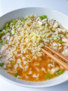 A bowl of ramen noodle soup with chopped green onions and pieces of meat, served with wooden chopsticks resting on the edge—perfect for any ramen noodle soup lover.
