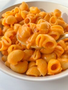 A close-up of a bowl of pasta shells coated in a creamy orange sauce, with a spoon lifting some pasta from the bowl—just like the famous Copycat Carbone Spicy Rigatoni.