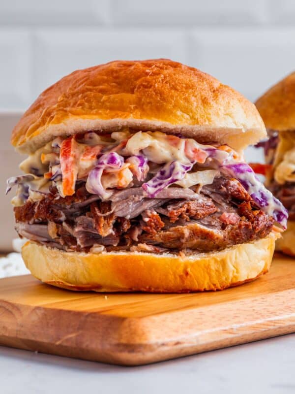 Pulled pork sandwich with coleslaw on a wooden board. The sandwich features tender, shredded pork topped with creamy coleslaw in a soft, golden bun.