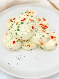A plate with a stack of round, fluffy Copycat Starbucks Egg-Bites with Ricotta, speckled with red bell peppers and green herbs, presented on a white plate and lightly garnished with chopped herbs.