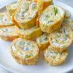 A plate of Zucchini Egg Roll pinwheels filled with cream cheese and diced vegetables, garnished with a sprig of fresh dill, displayed on a white plate.