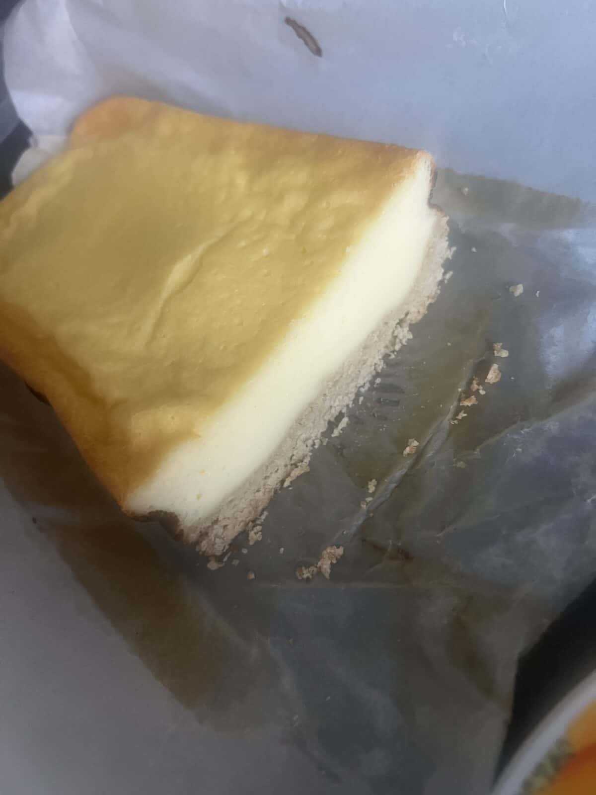 A close-up view of a partially eaten slice of cheesecake with a golden top and a thin crust, resting on parchment paper, reminiscent of a homemade 3 Ingredient Yogurt Cake.