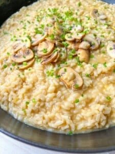 A close-up of creamy mushroom risotto in a dark bowl, topped with sliced mushrooms and fresh chopped chives—an inviting dish that's perfect for any Simple Risotto Recipe.